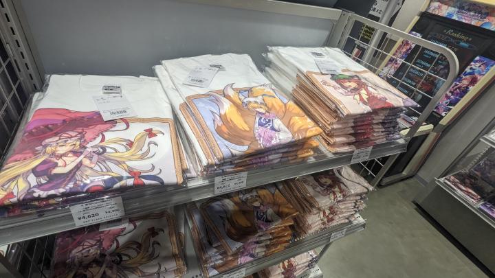 Store shelfs full of white t-shirts with illustrations depcting Touhou characters printed on.